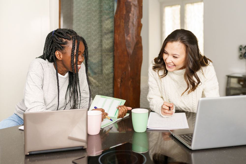 Two women sitting at kitchen table doing work on their pcs