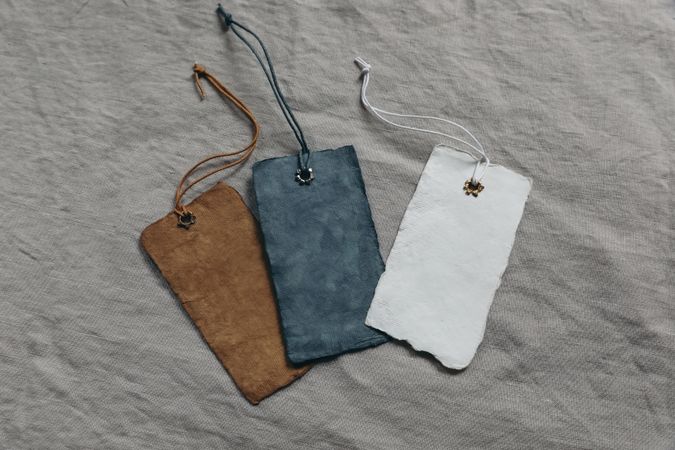 Set of colorful cotton paper tags mockups with metal rivets and strings for clothes, gifts or products. Blank space for text, logo. Branding, business. Linen table cloth background, flatlay, top view.