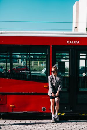 Woman with tablet in stylish suit standing nearby red bus