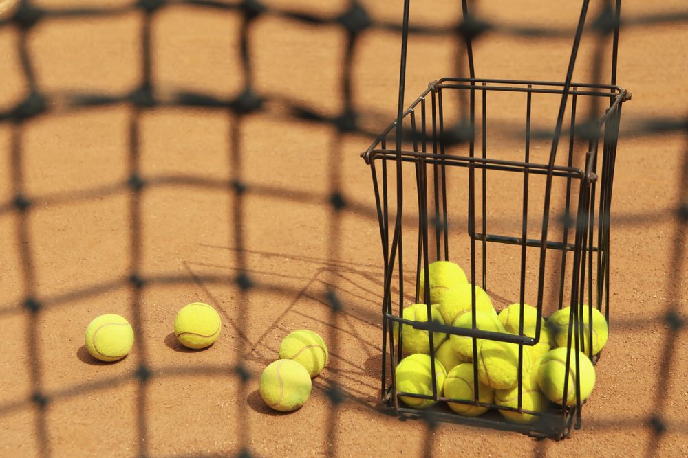 Tennis net against clay court with basket with balls
