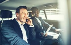 Two businessmen smiling and working while being driven in a luxury vehicle
