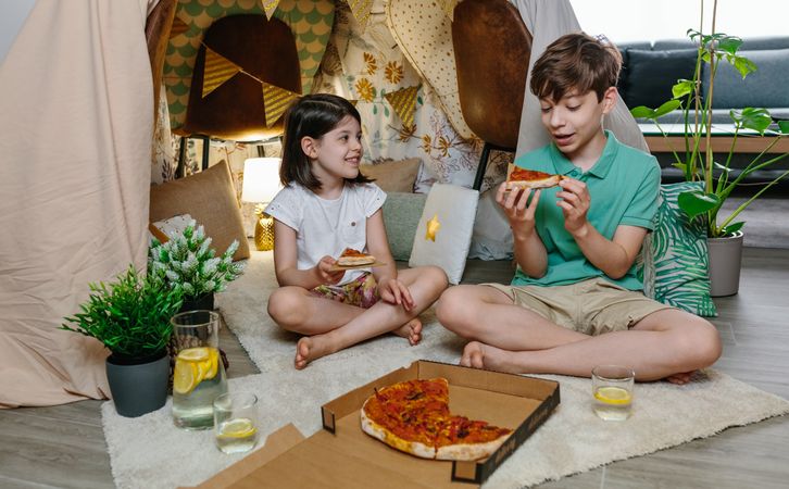 Children eating pizza and lemonade while camping at home