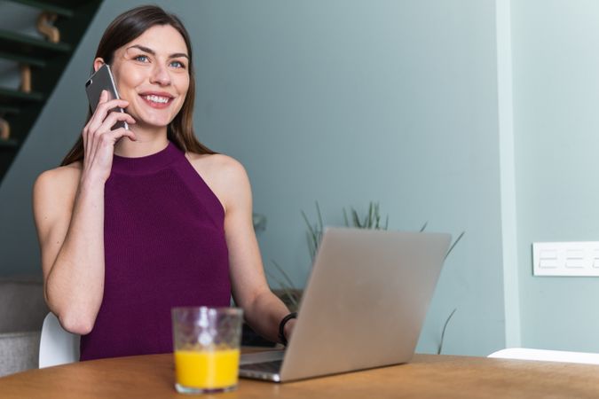 Smiling woman using smartphone and sitting at table with laptop