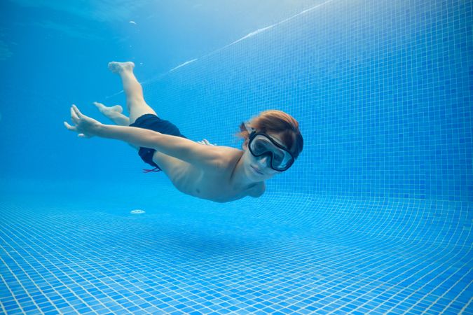 Boy in shirts and goggles swimming in blue pool