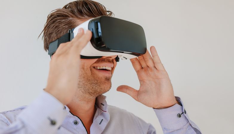 Shot of happy young man wearing virtual reality goggle against grey background
