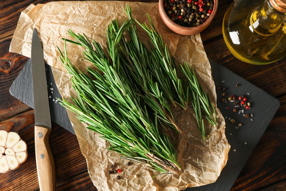 Composition with rosemary, oil, pepper, garlic and knife on wooden table, top view