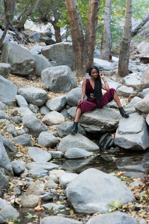 Confident woman sitting by a creek in front of trees in the mountains