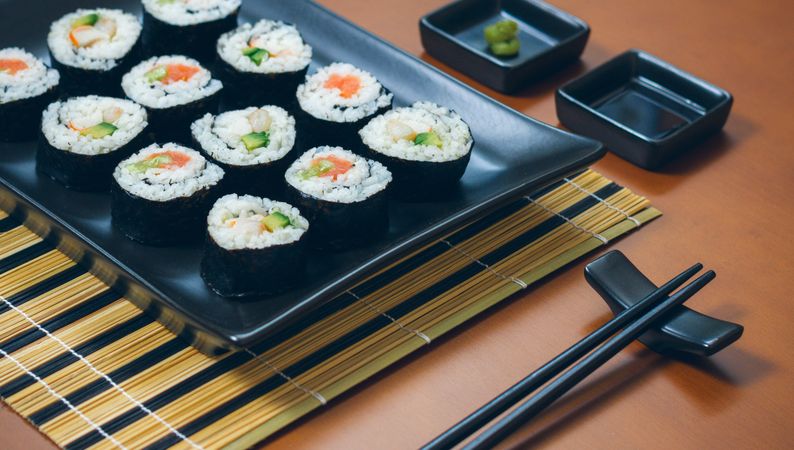 Fresh sushi rolls plated on rectangular tray on mat with chopsticks