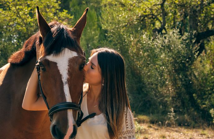 Tender woman kissing horse in muzzle
