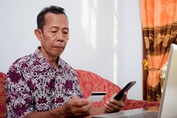 Asian male holds and looks at the blank credit card doing payment online