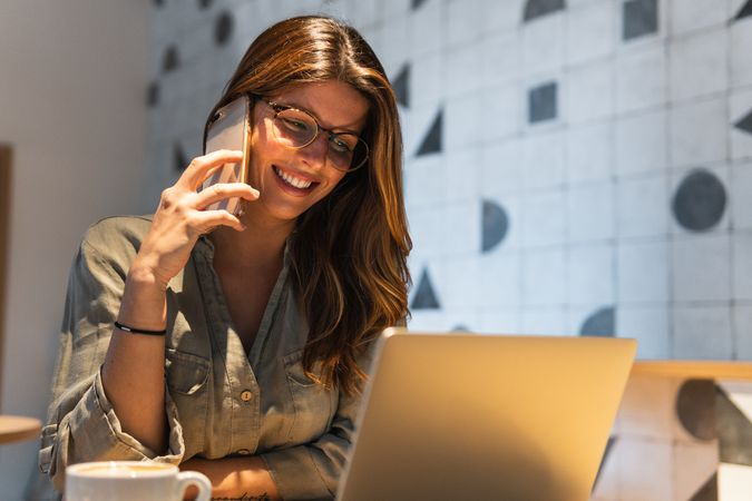 Woman speaking on smartphone against laptop in cafeteria