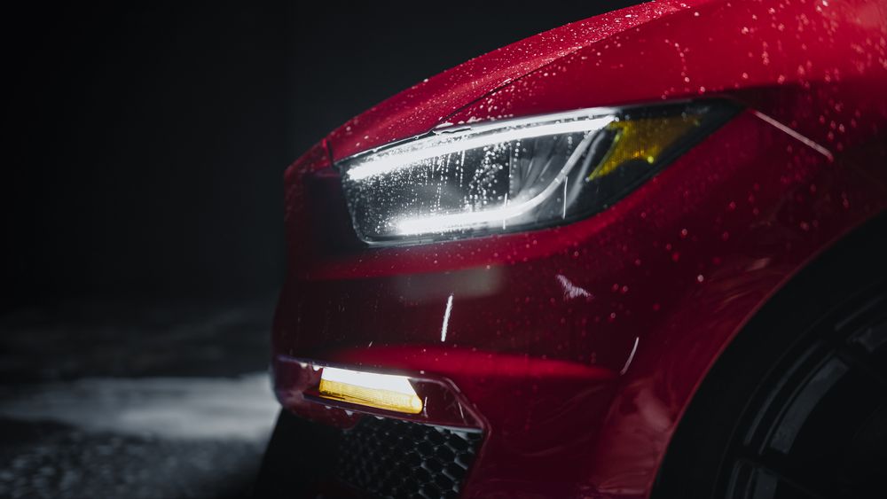 Modern Red Performance Vehicle with LED Headlights is Being Cleaned at a Dealership Car Wash.