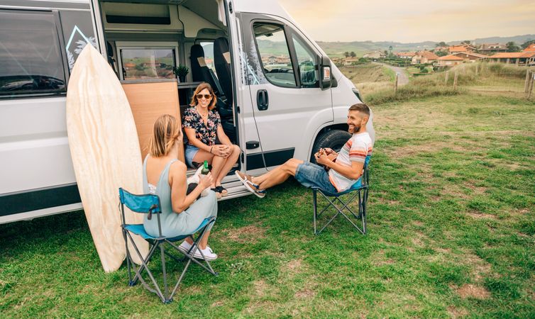 Three happy people sitting and talking in front of parked motorhome