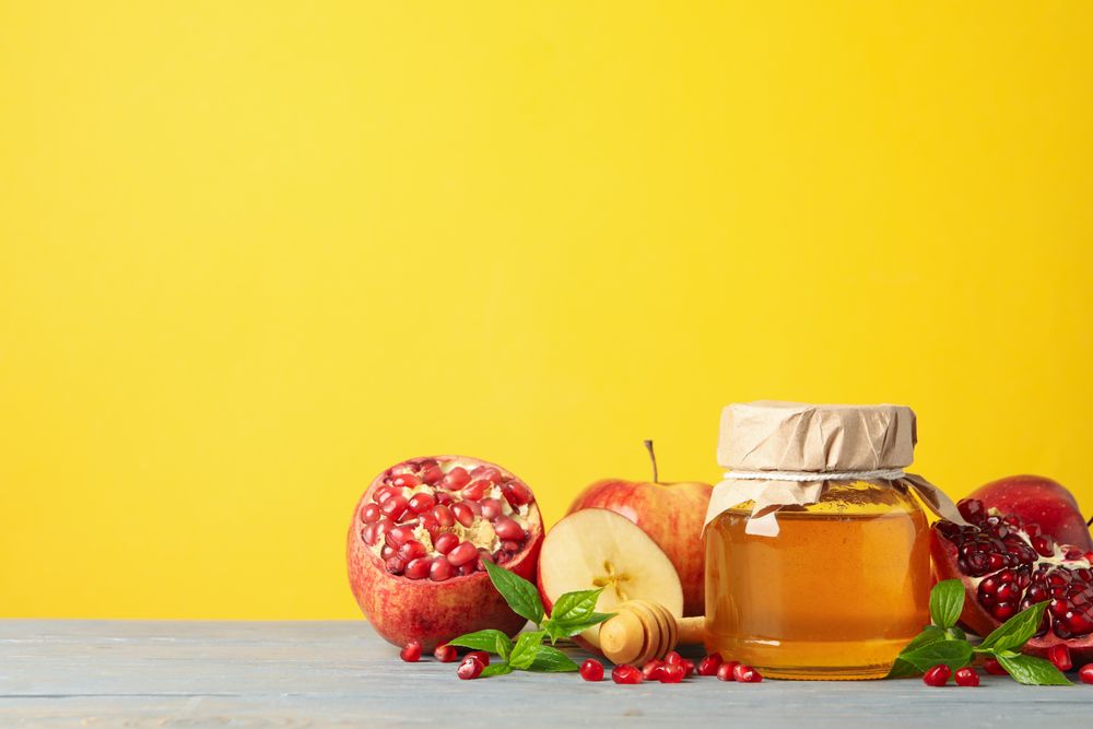 Apples, pomegranate, and honey pot in bright yellow room with copy space