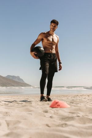 Athletic man standing with weighted ball at a beach