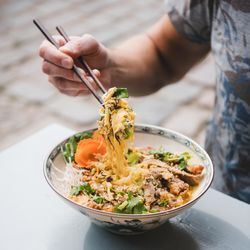 Man eating noodles at Vietnamese restaurant with chopsticks, square crop