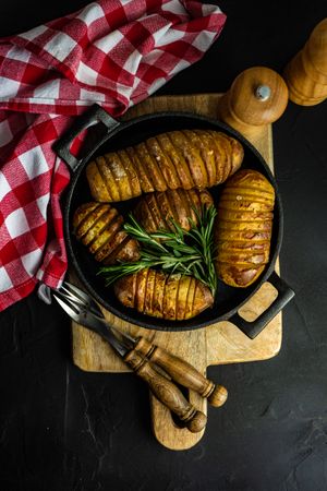 Top view of baked potato fans with rosemary in iron cast pot on kitchen counter