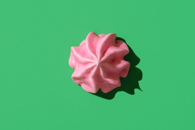 Pink meringue cookie minimalist on a green background, top view