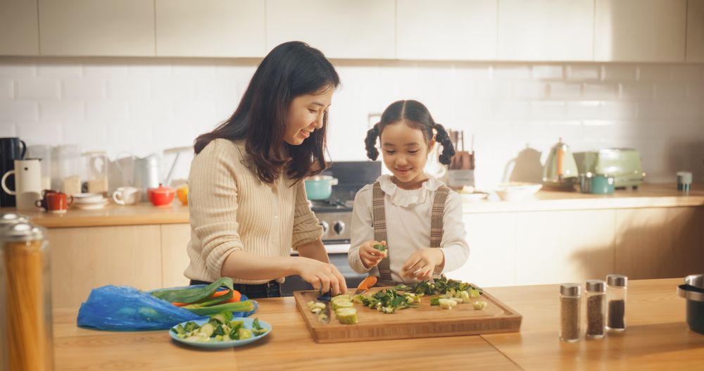 Mother Teaching her Little Girl How to Cut Vegetables.