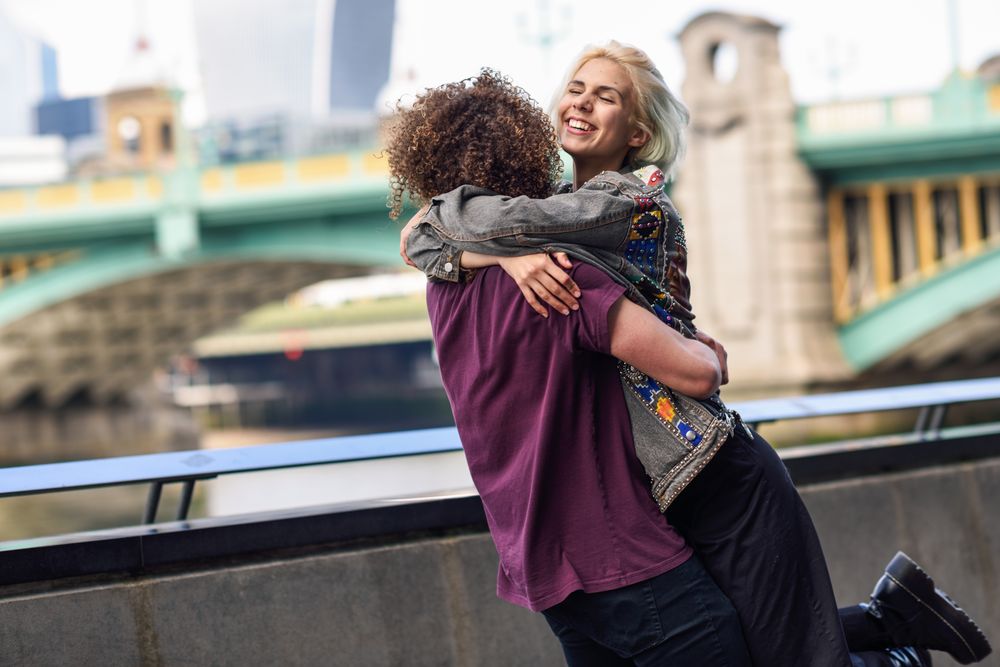 Man lifting up his smiling girlfriend on riverwalk with bridge in background