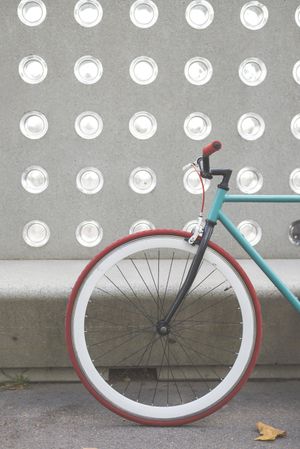 Red and green bike parked in front of patterned cement wall, vertical