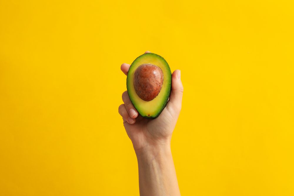 Female hand hold avocado on yellow background