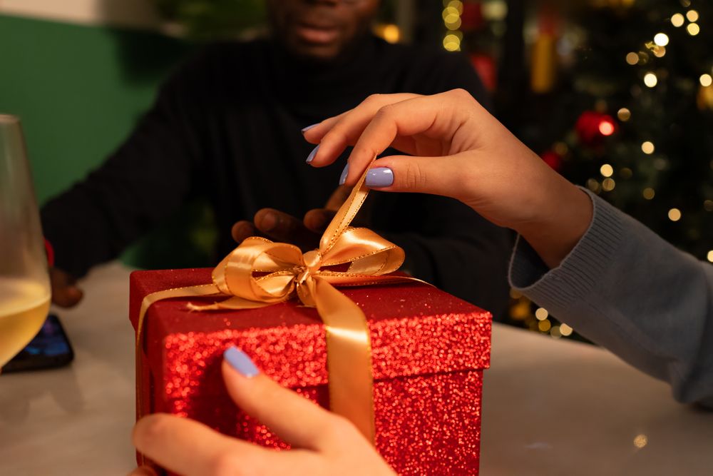 Close-up of a woman's hands opening a red Christmas gift box at a party