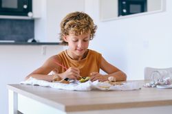 Content preteen boy painting stone at table
