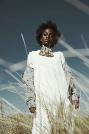 Woman in light dress and denim jacket standing under blue sky