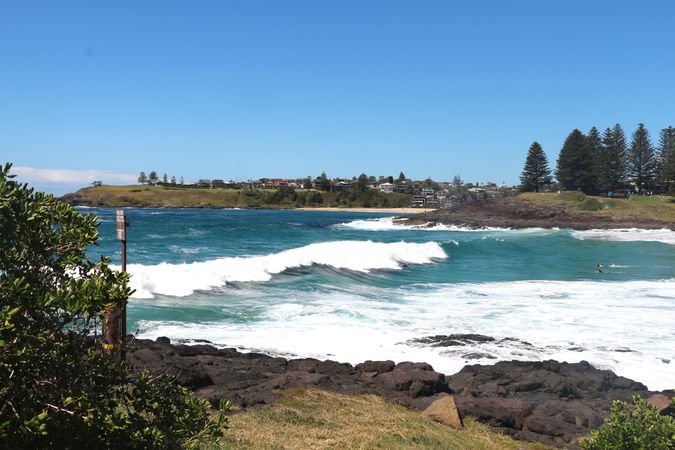 Coastal view with waves crashing against rocks under clear blue sky at a serene beach location