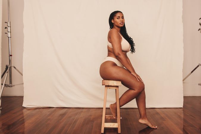 Body positive young woman looking at the camera while sitting on a chair against a studio background