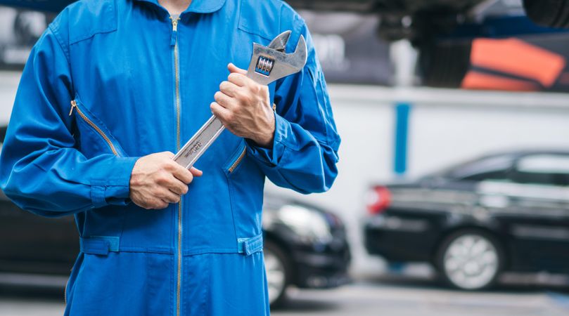 Close up of white male mechanic holding wrench at auto garage