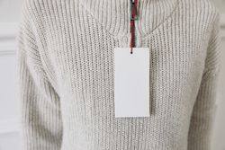 Blank paper price tag, label mockup on beige knitted sweater