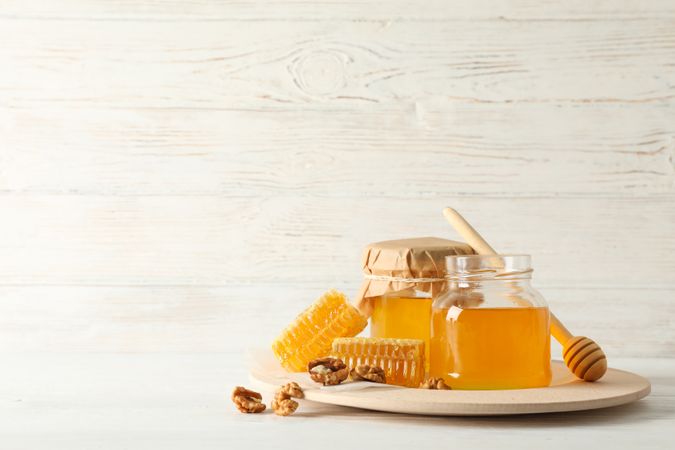 Honeycombs, walnuts, dipper and jars with honey on wooden background, copy space