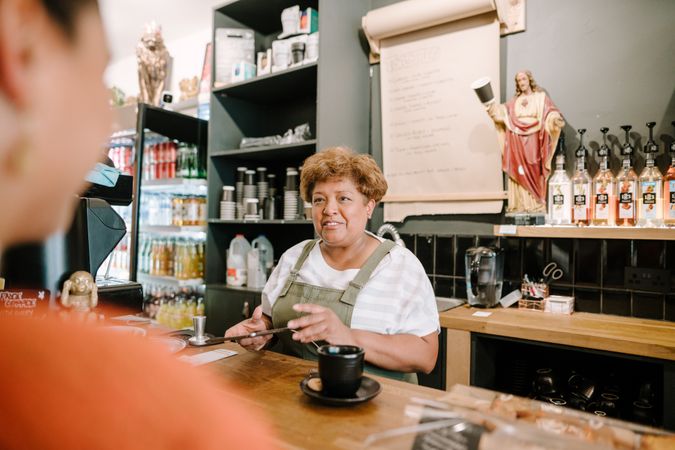 Older Black woman ringing up order on digital tablet in cafe