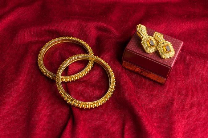 Beautiful shiny golden bangles and diamond studded traditional earrings on a red velvet background