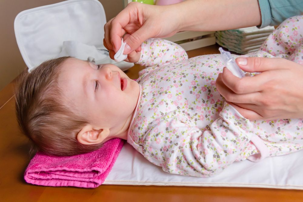 Mother cleaning annoyed baby's eyes with cotton
