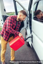 Male in red checkered shirt filling up petroleum in van with gas can, vertical 5zqmA0