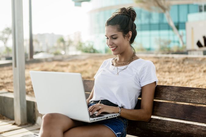 Woman working on her laptop sitting on a wooden bench