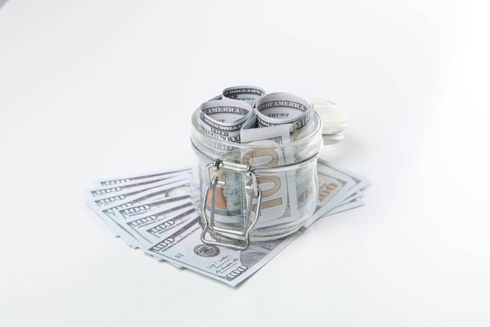 Stacks of American cash money in glass jar on light background