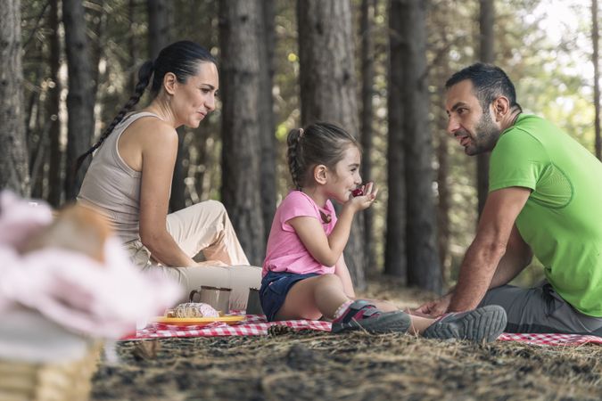 Happy family enjoying a healthy fruit snack during a picnic in the forest.