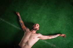 Young bearded guy with tattoos on hands lying on lawn