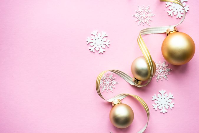 Gold Christmas baubles and snowflake decorations on pink background