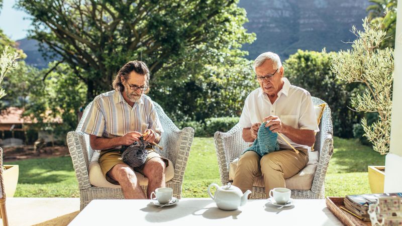 Two older men sitting in patio and knitting