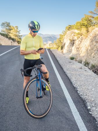 healthy man with smartphone after cycling in a mountain road in a sunny day