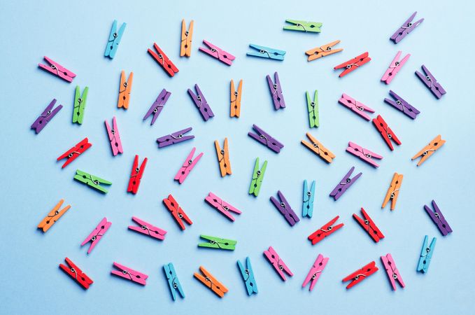 Scattered rainbow colored clothes pins on light blue background