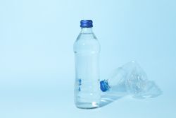Full & crushed water bottle in blue room, copy space