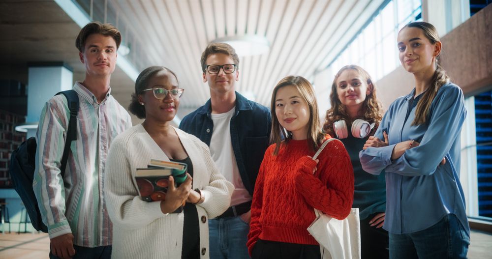 Diverse Group of Students Standing Together in Modern University Hallway, Smiling Confidently.
