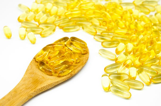 Fish Oil Capsules on Wooden Spoon and Pile