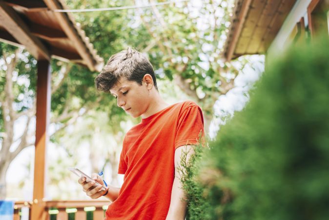 Profile of a happy male teen texting on a smart phone in the yard